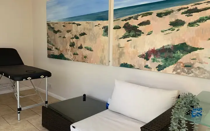 A white sofa and treatment couch in the TweakBoutique clinic beneath a painting of the beach
