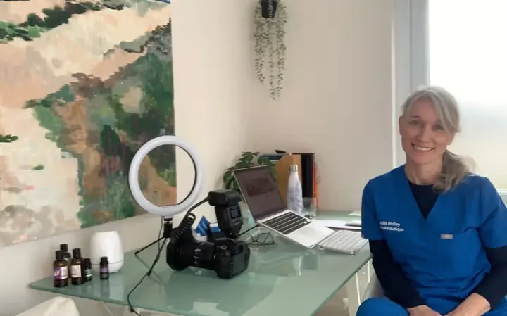 Dr Julie Ridley smiling at her desk in the clinic, wearing TweakBoutique scrubs