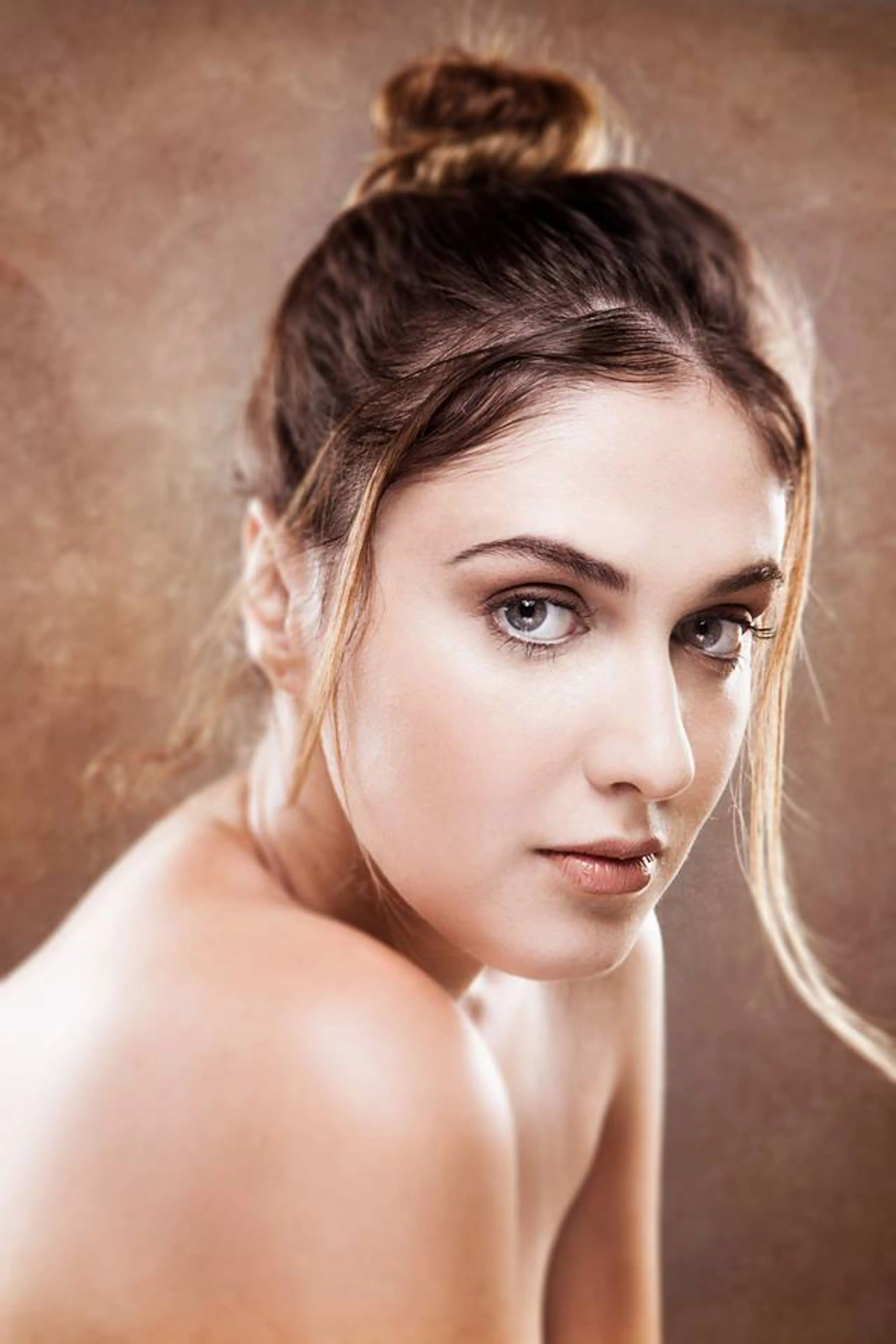A woman with her hair up looking over her shoulder against a warm brown backdrop