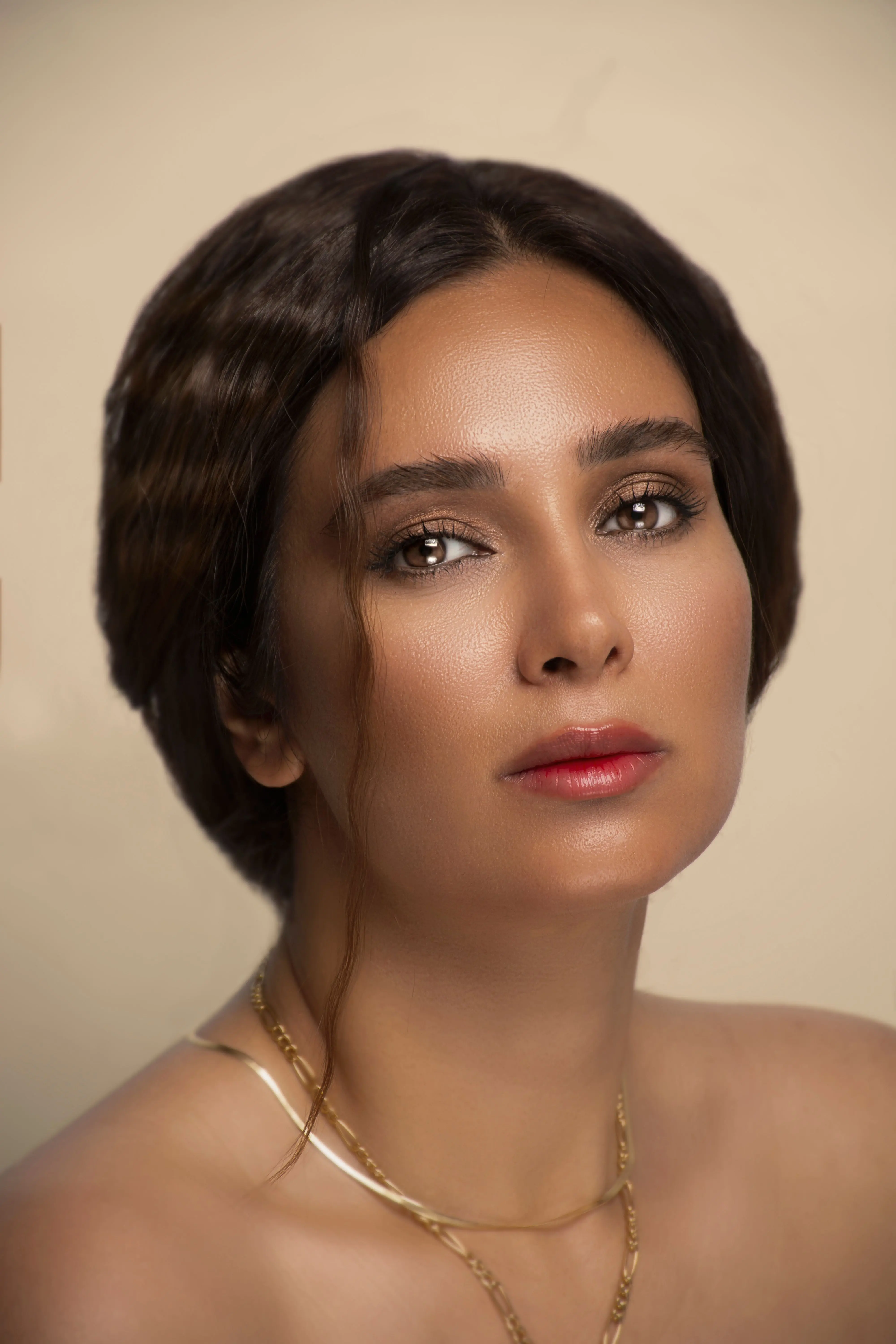 A woman with dark hair and gold necklaces looking directly at the camera