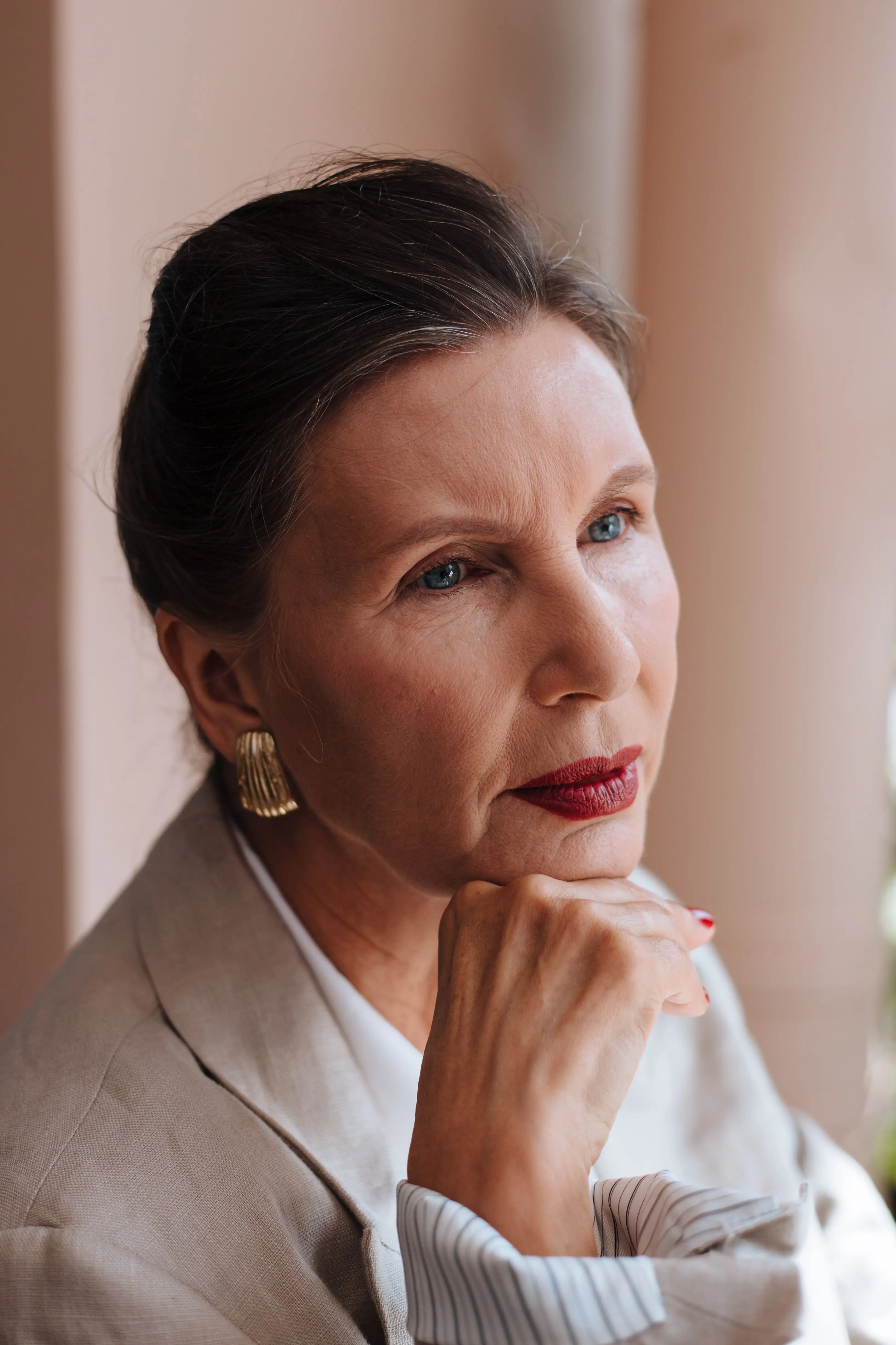 A woman in her fifties in a cream jacket resting her chin on her hand