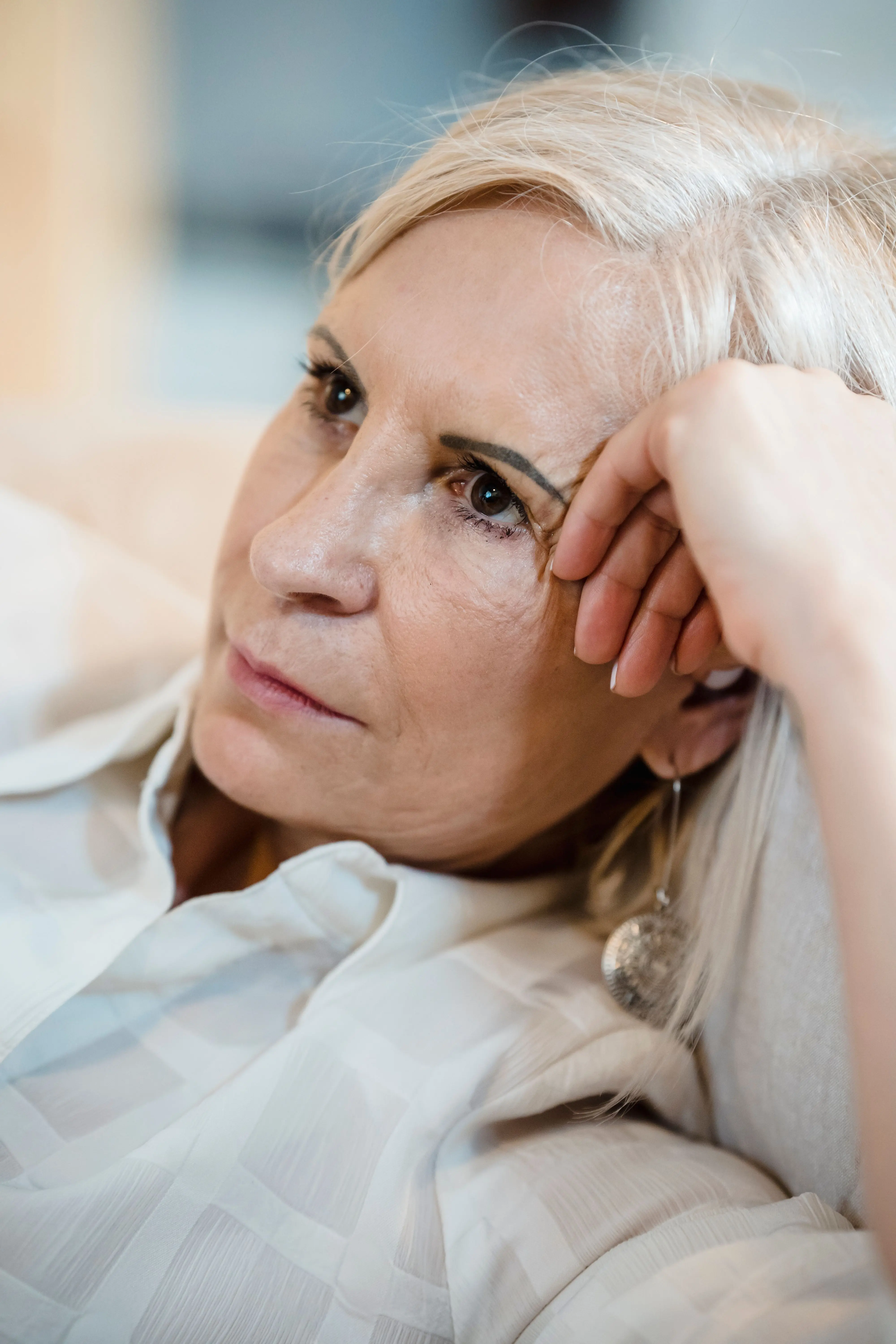 A woman in her fifties resting her hand in her hair, looking calmly at the camera