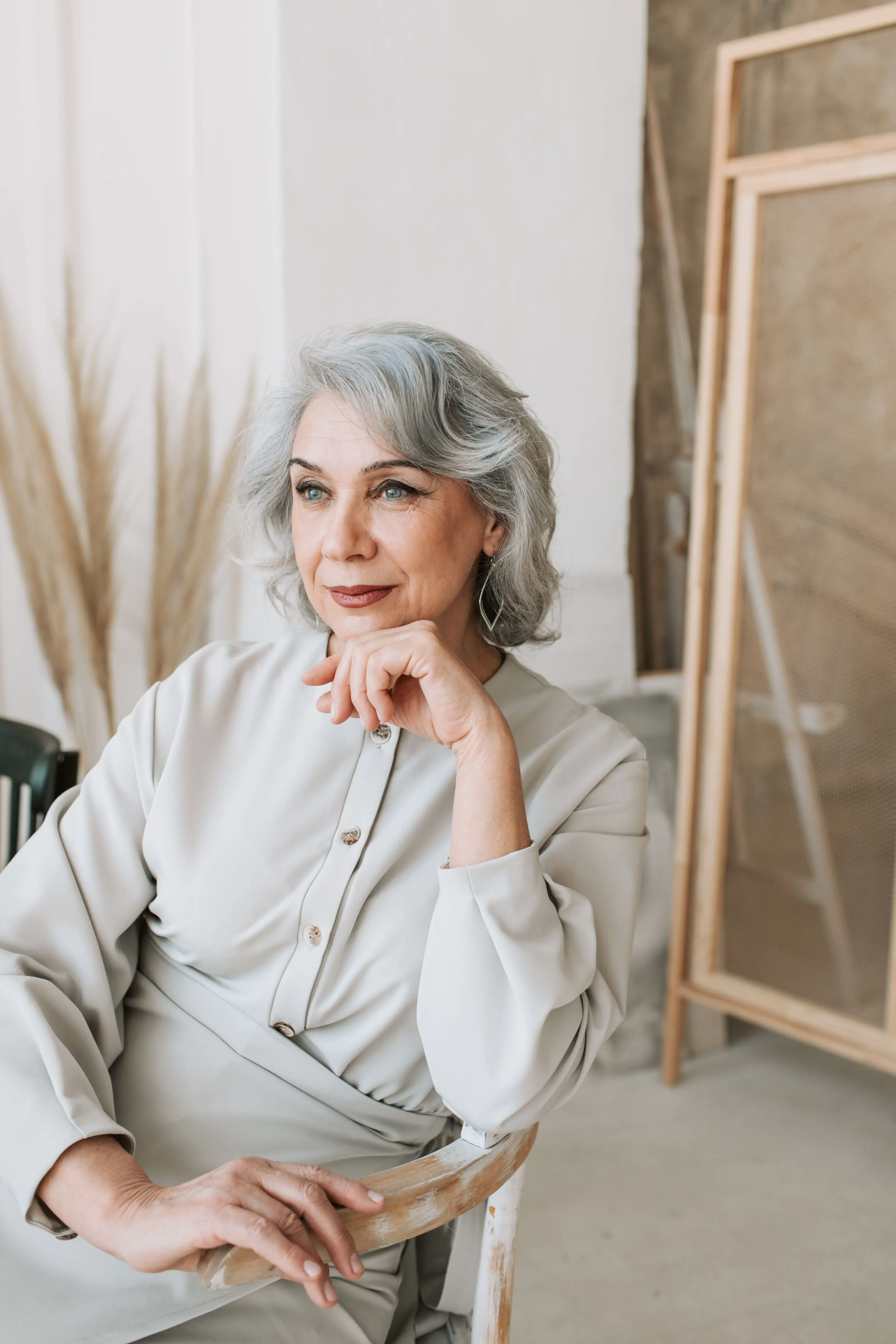 A woman with silver hair seated in a bright room, hand resting under her chin