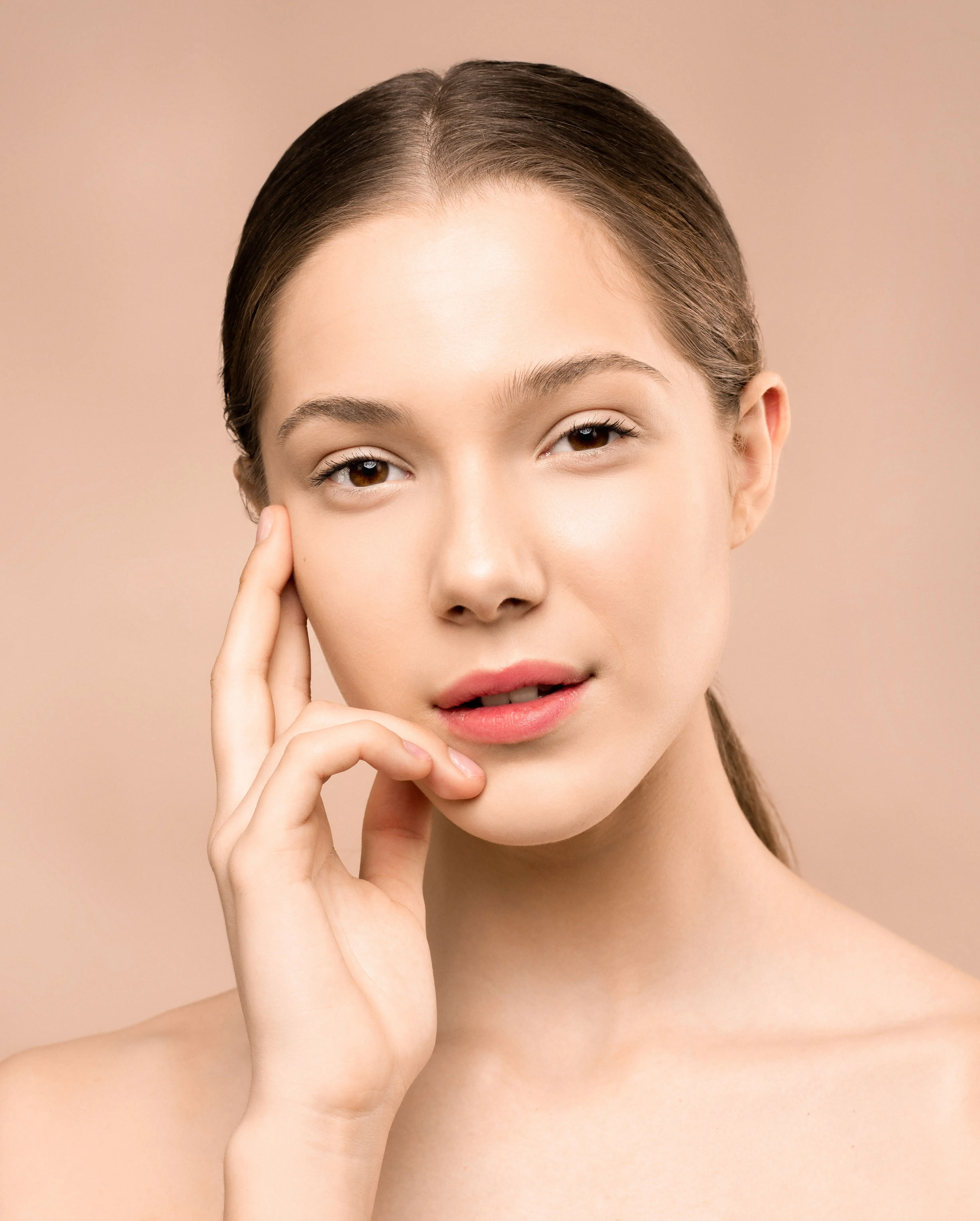 A woman with clear, natural skin resting her hand against her cheek