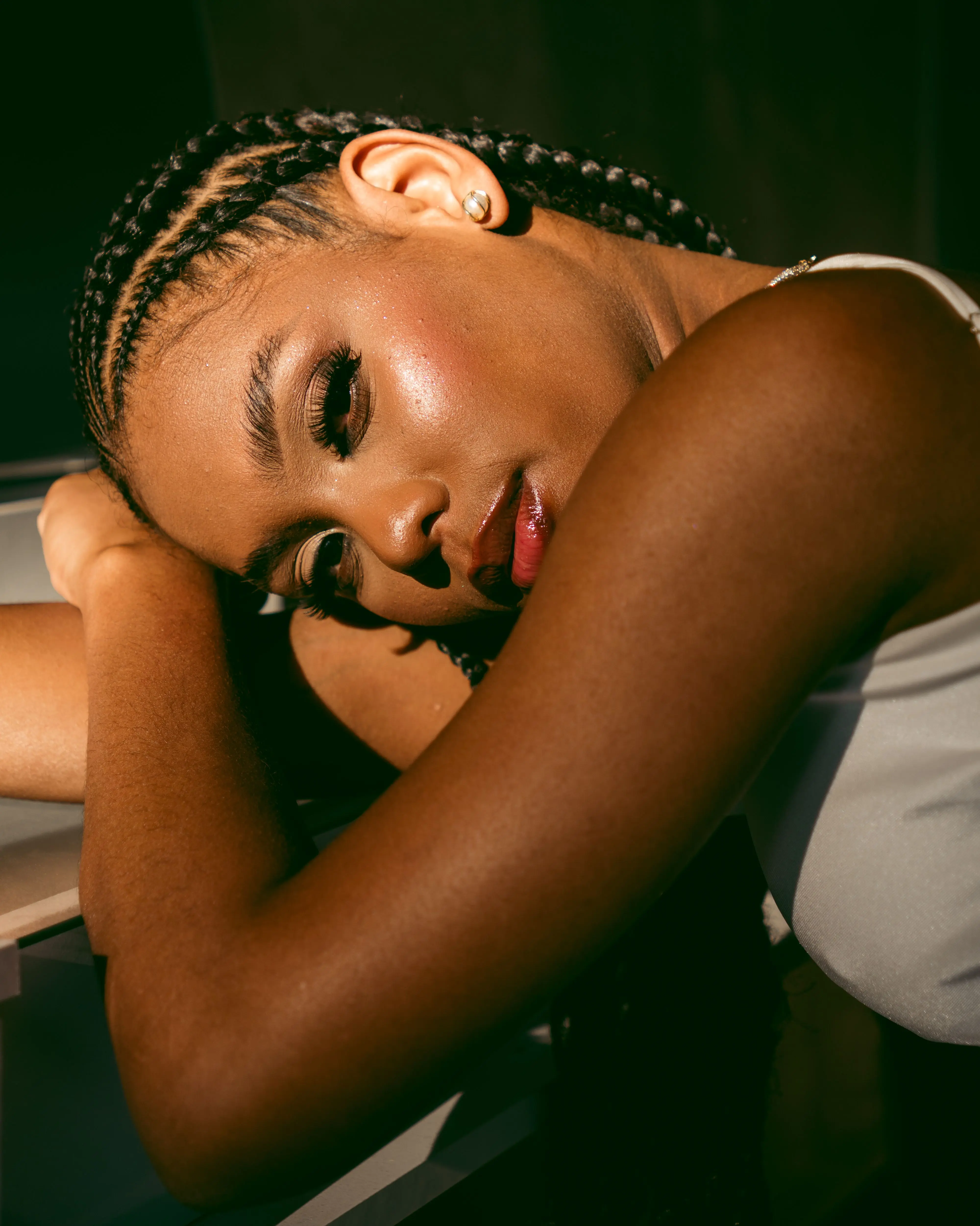 A woman with braided hair resting her head on her arm in warm indoor light