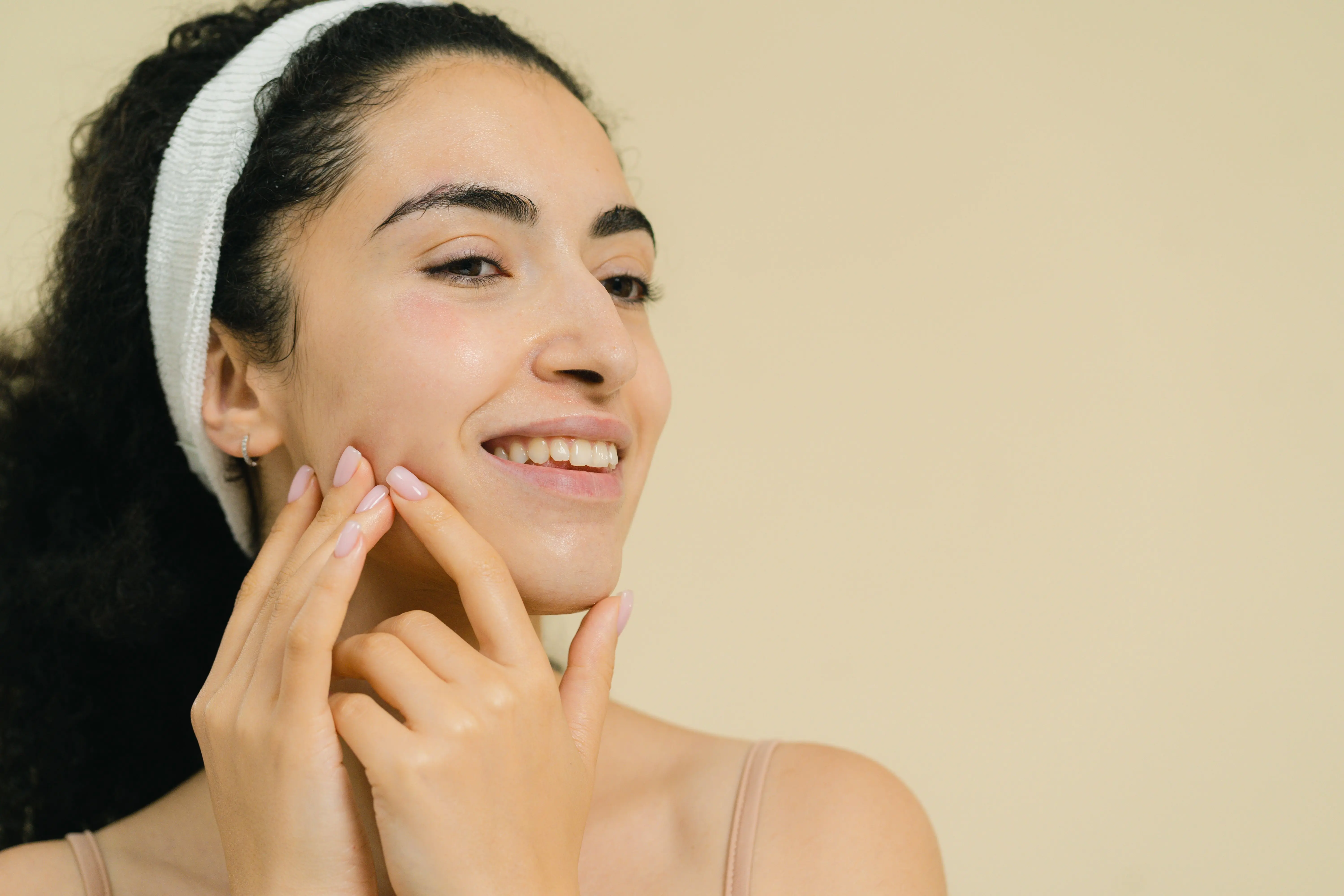 A woman with a headband smiling and holding her fingertips to her jaw