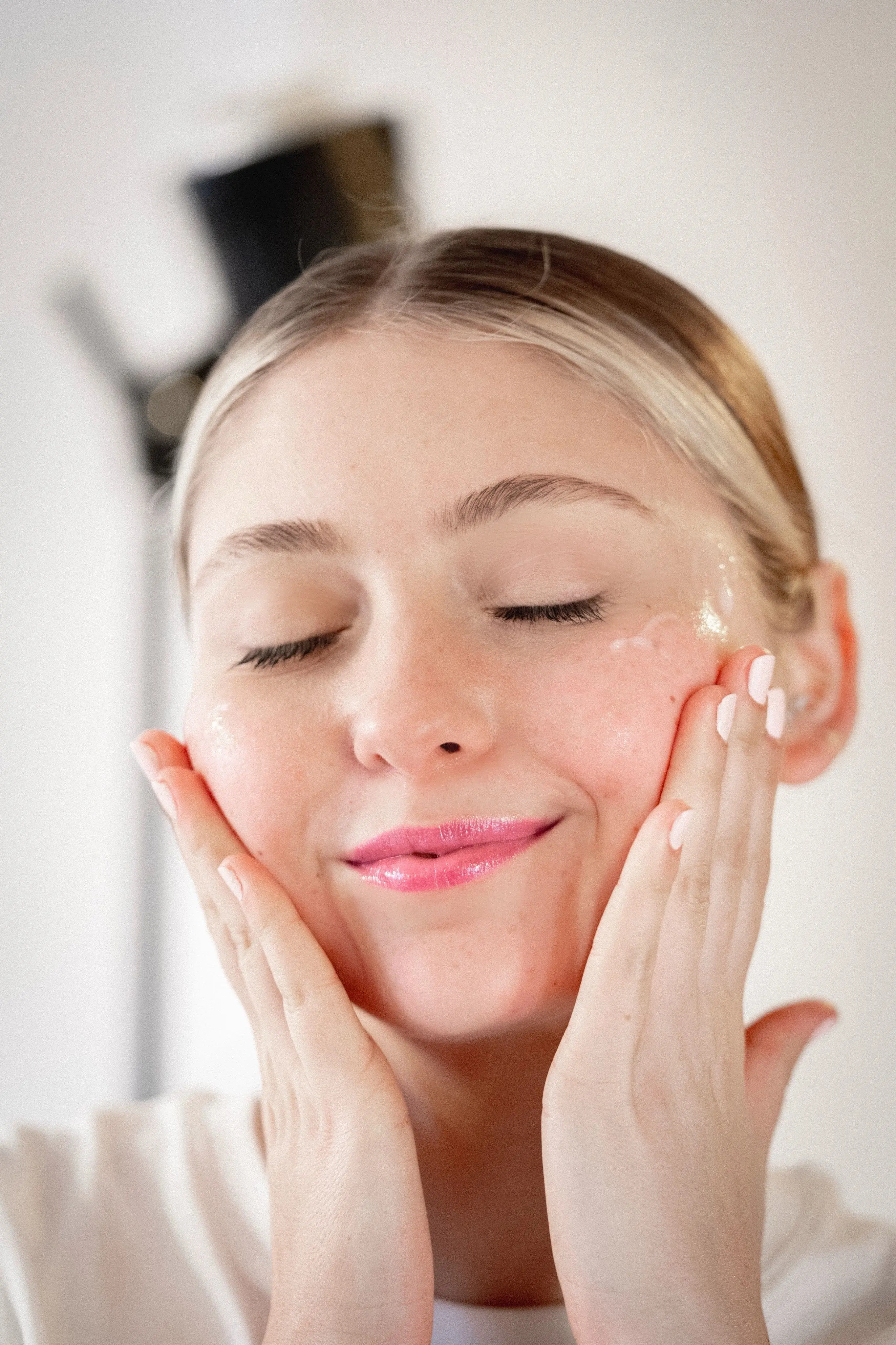 A woman with her eyes closed applying skincare cream to her cheeks