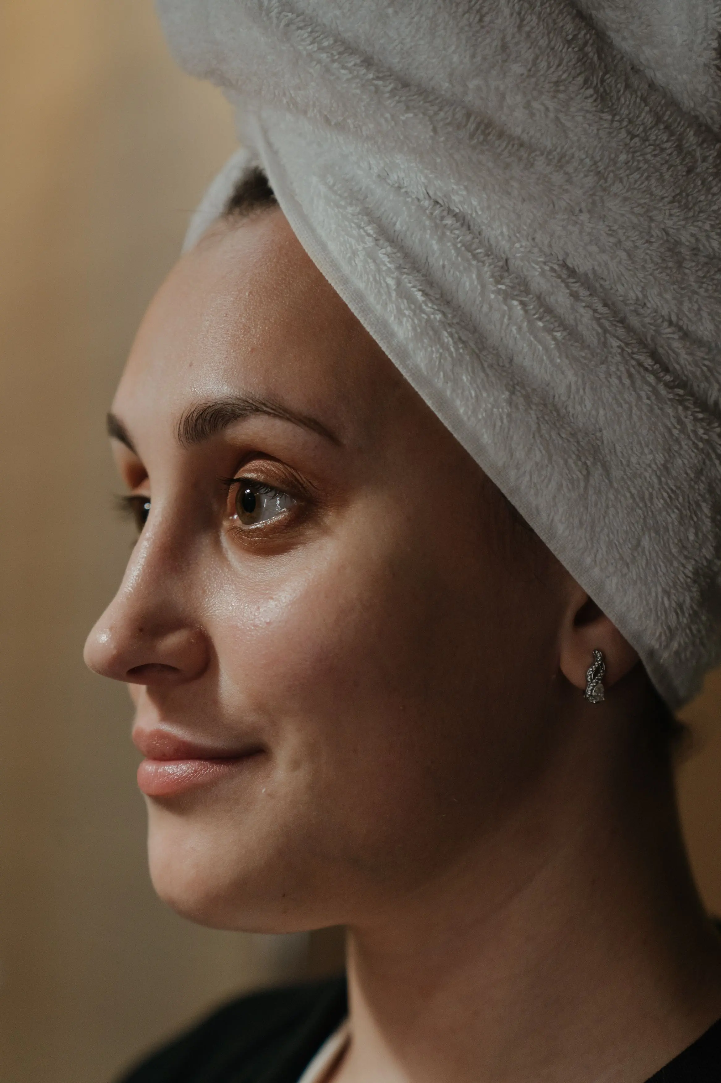 A profile portrait of a woman with a towel wrapped around her hair and fresh, bare skin